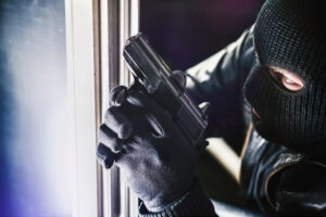 Masked burglar with pistol gun breaking and entering into a victim's home