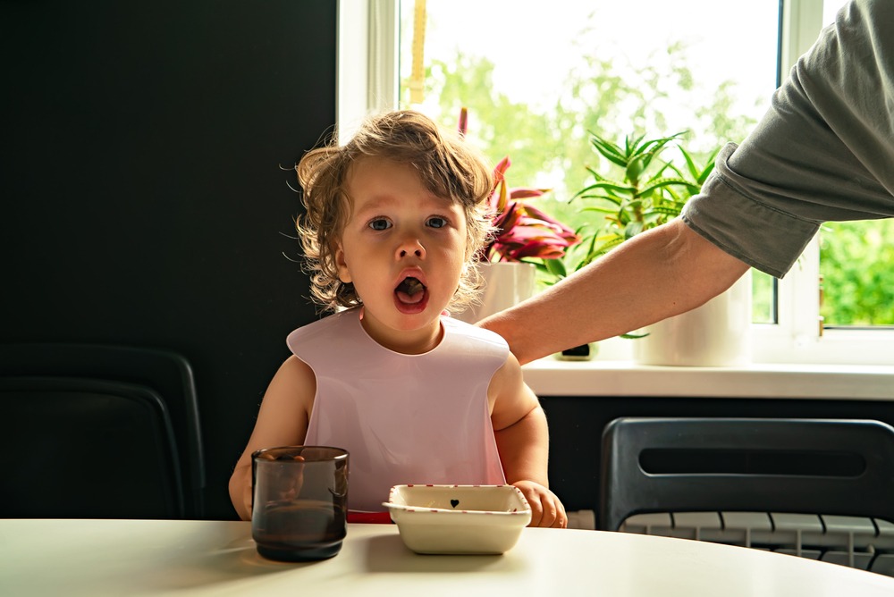 A small child chokes on food while a parent pats her back.