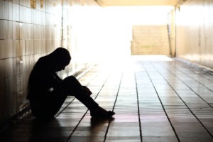 Silhouette of a teenager sitting down in a hallway looking depressed.