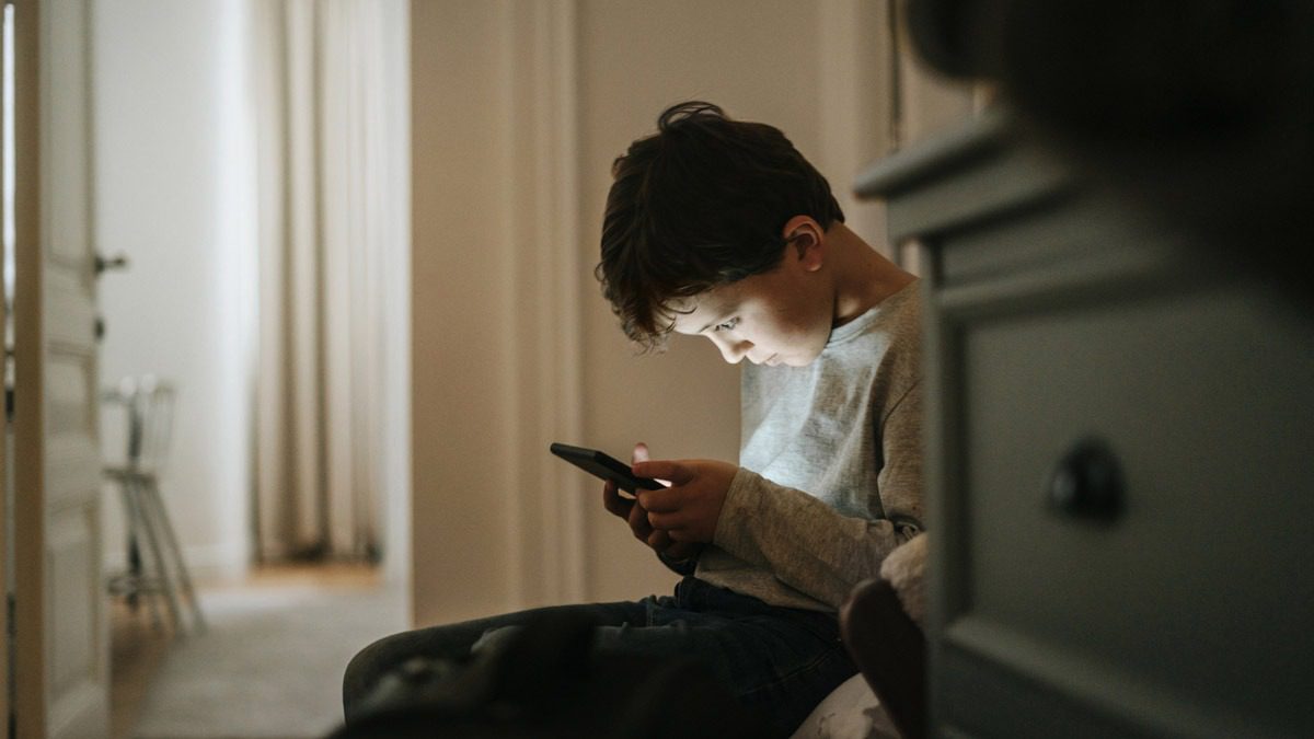 young-boy-sitting-down-with-face-lit-up-from-phone