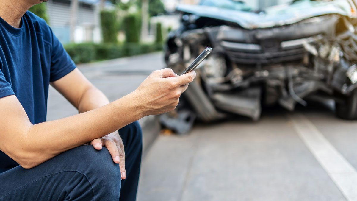 Man holding phone after accident with crashed car in background