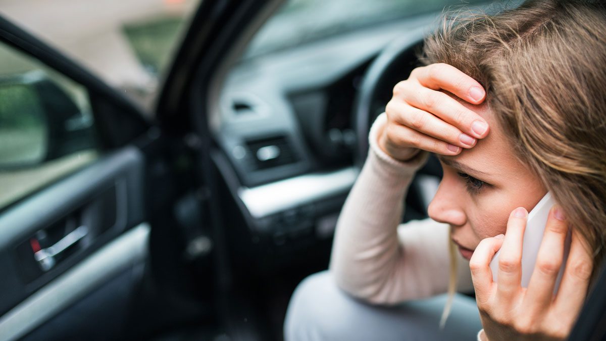 Young woman in the damaged car after a car accident, making a phone call
