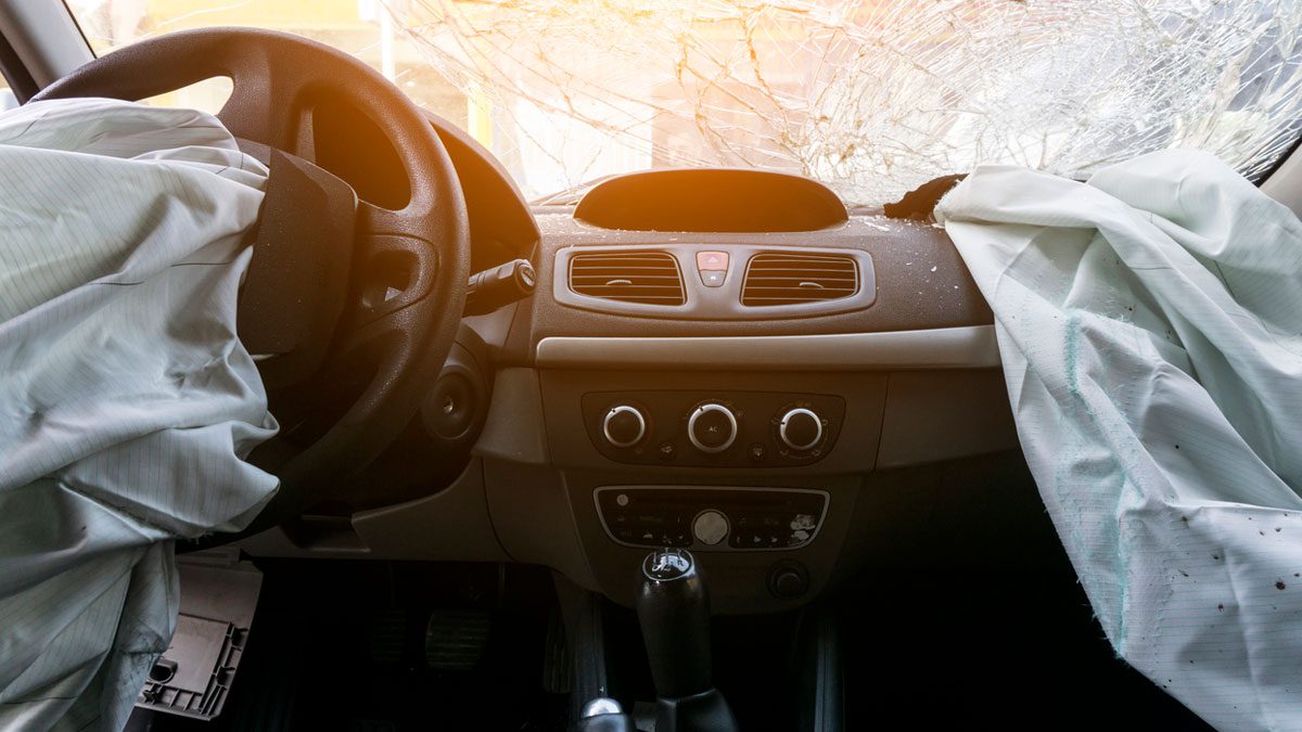 inside of car after accident, showing broken windshield and deployed airbags