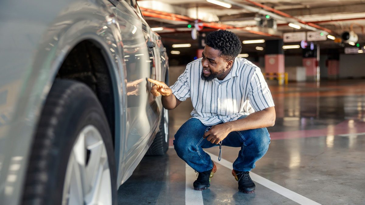 man-examining-damage-on-parked-car