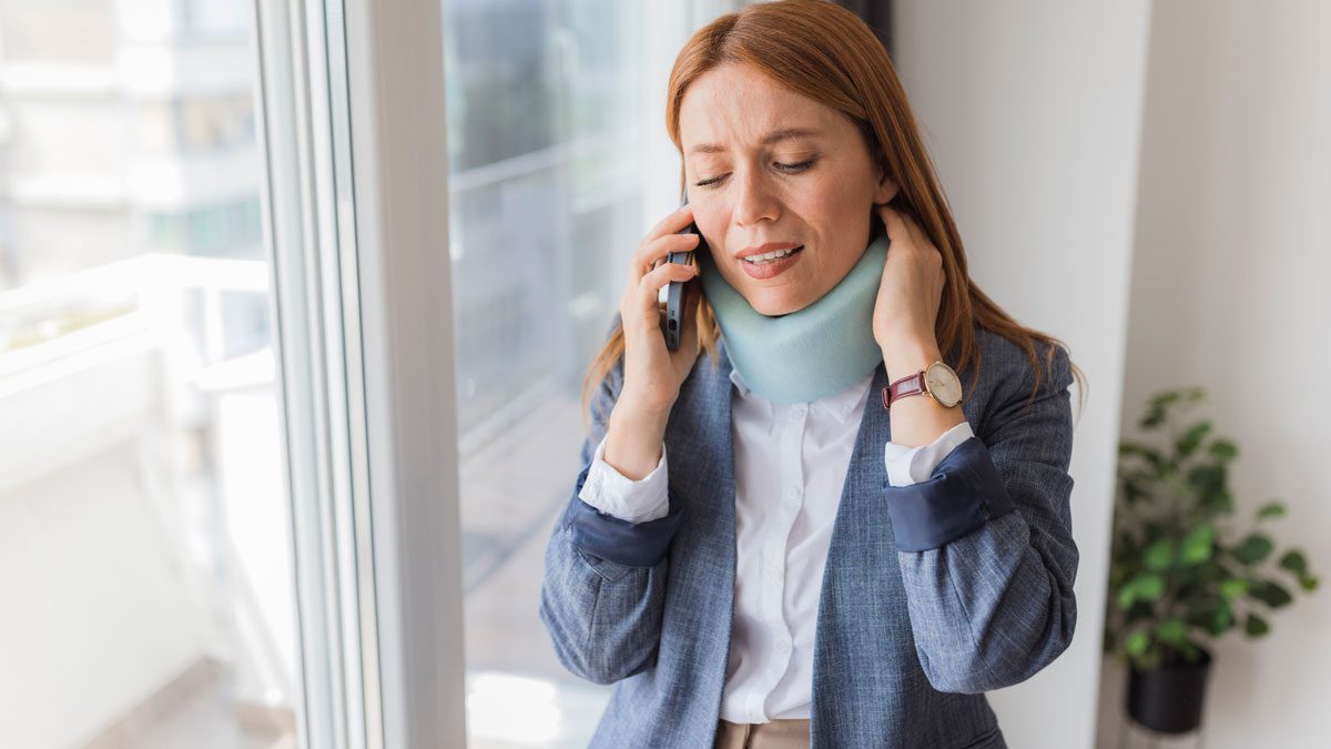 woman wearing neck brace talking on phone by the window