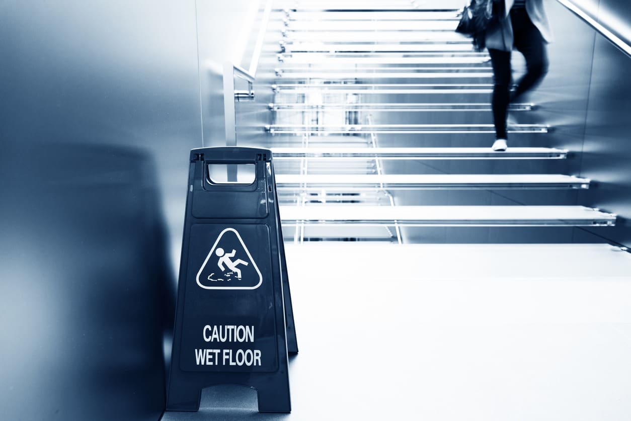 individual walking down a flight of stairs with a wet floor sign at the bottom