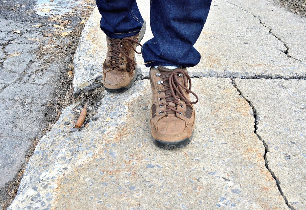 view of person wearing work boots and walking on uneven sidewalk
