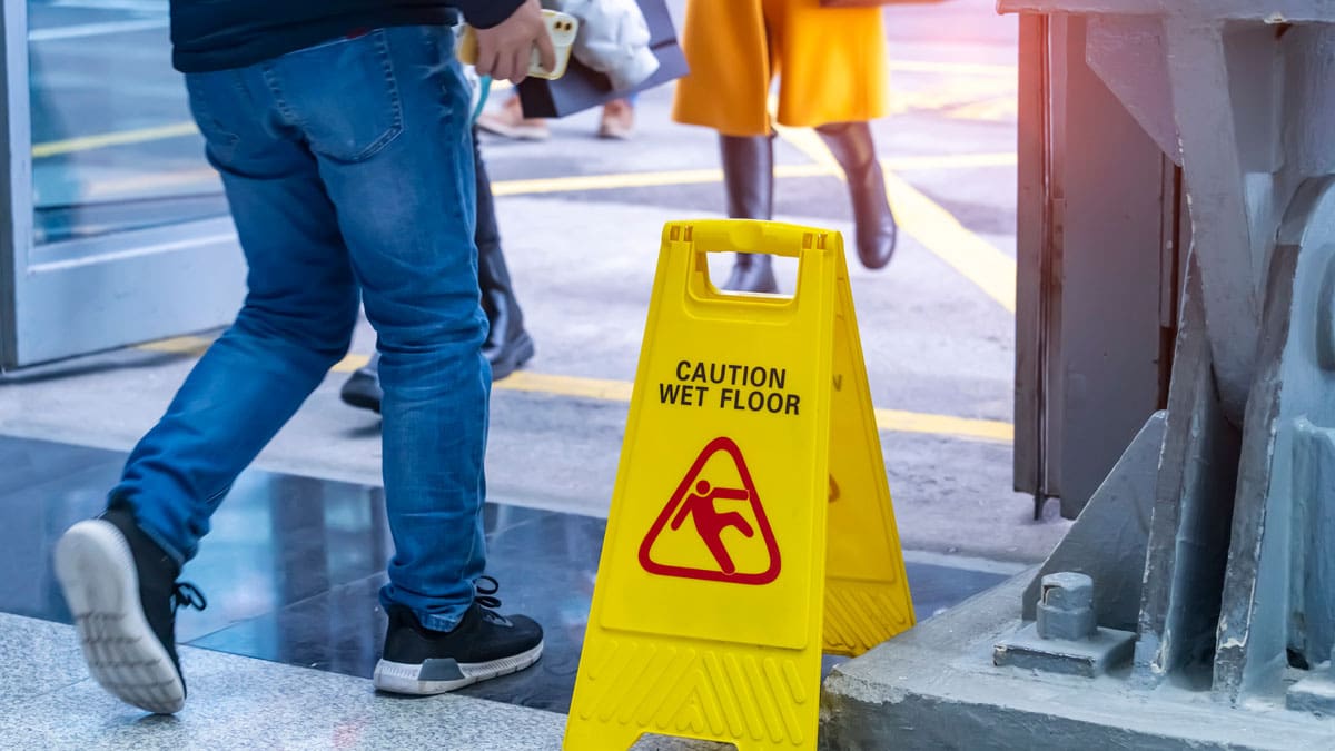 caution-wet-floor-sign-on-a-sidewalk-as-people-walk-past
