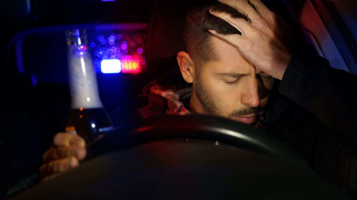 driver-holding-his-head-with-police-lights-flashing-behind-the-car