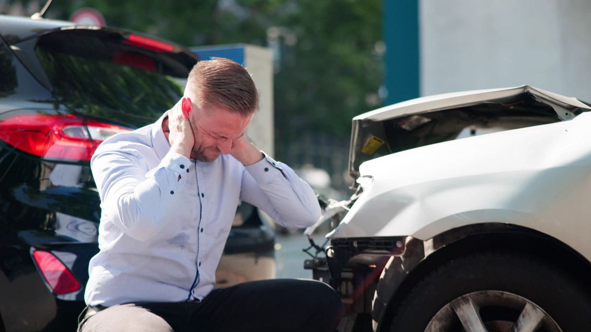 man-holding-his-neck-while-crouched-beside-a-wrecked-car