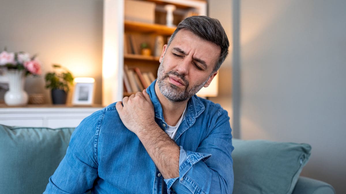 man-sitting-on-a-couch-holding-his-shoulder