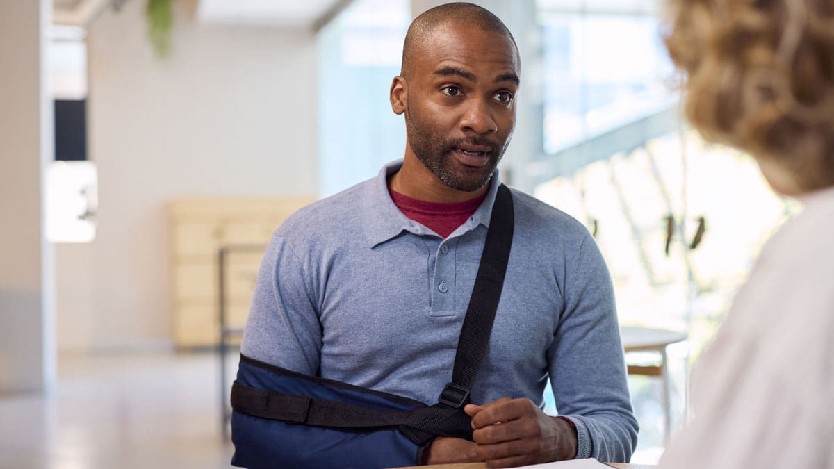 man-with-his-arm-in-a-sling-talking-with-someone-in-an-office
