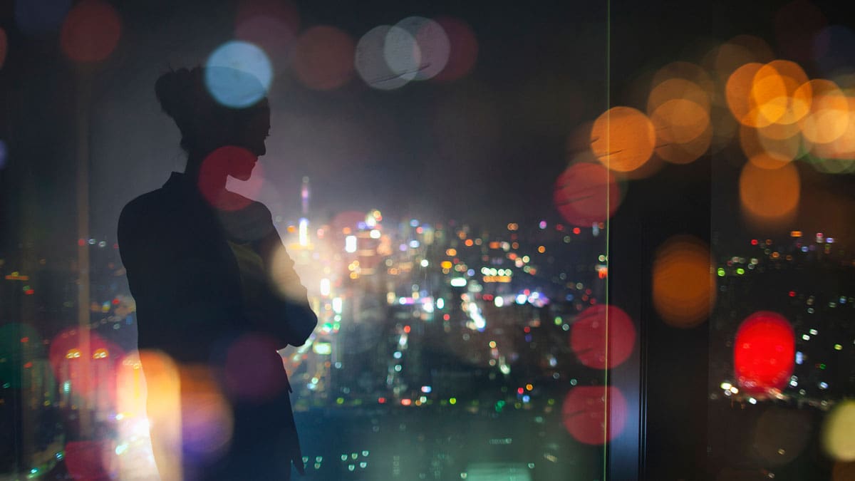 person-standing-at-a-window-looking-out-at-city-lights-at-night