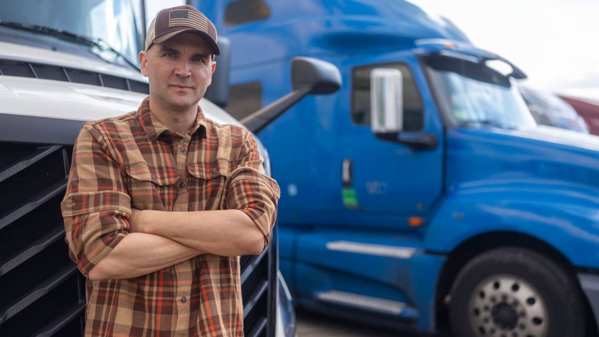 truck-driver-standing-with-his-arms-crossed-in-front-of-a-blue-semi