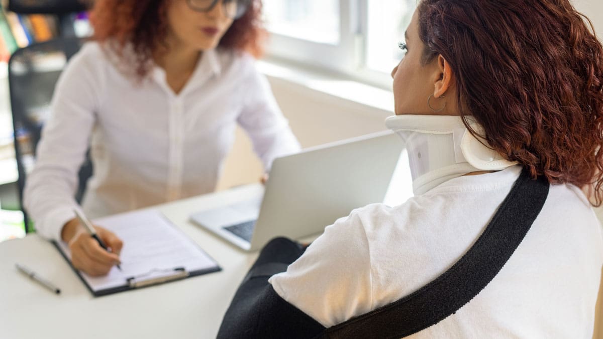 two-women-meeting-across-a-desk-with-a-clipboard-and-laptop