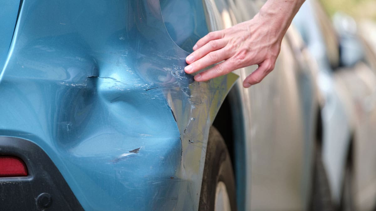 hand-touching-a-large-dent-in-the-side-of-a-blue-car