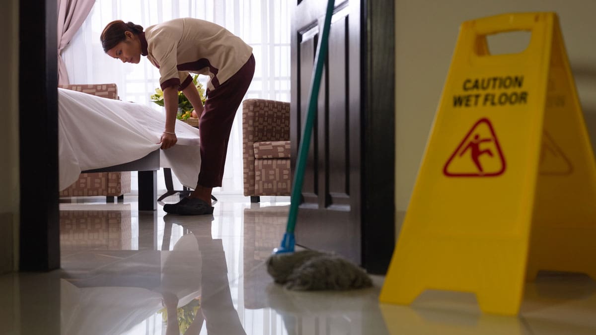 housekeeper-cleaning-a-hotel-room-beside-a-caution-wet-floor