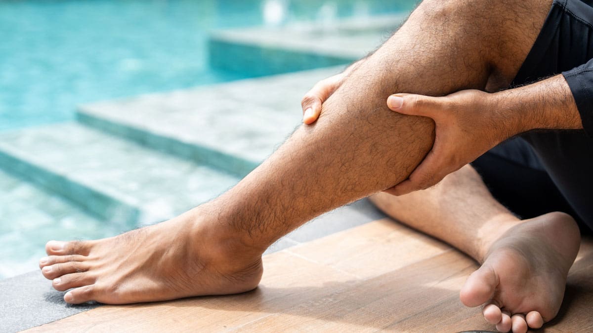 person-holding-their-ankle-while-sitting-at-the-edge-of-a-pool