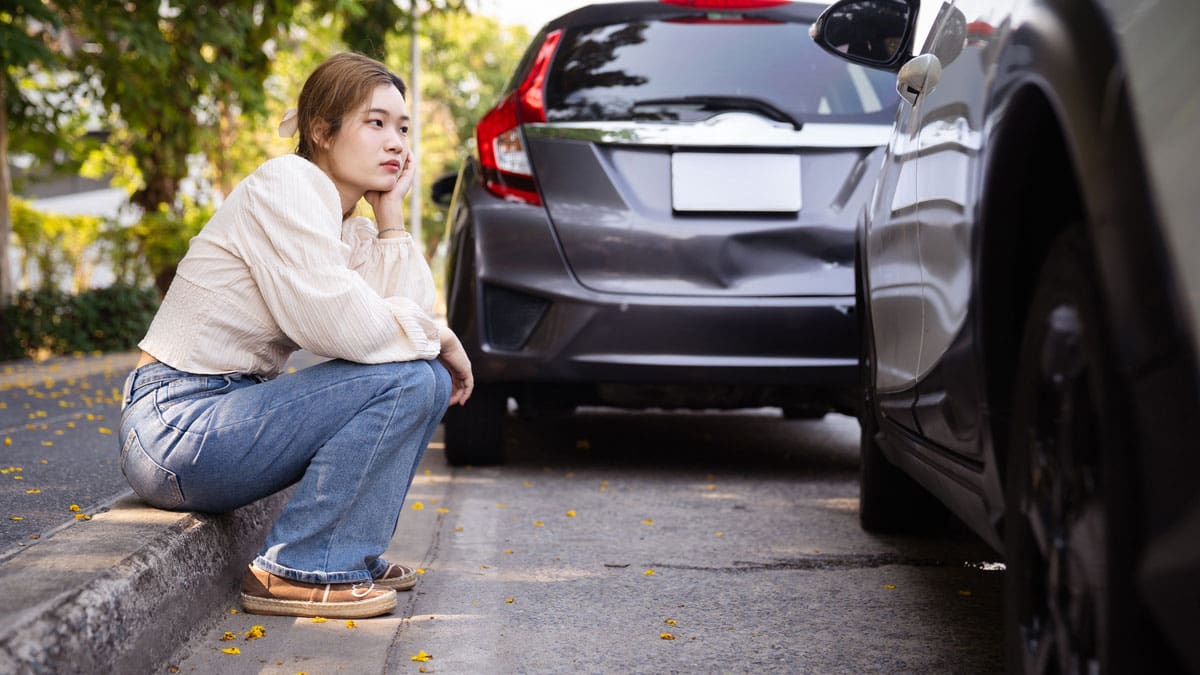 woman-crouched-at-the-curb-beside-a-damaged-car