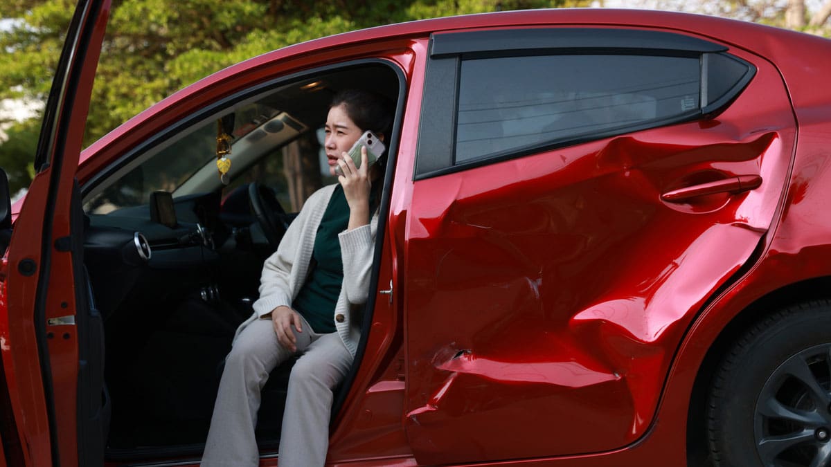 woman-sitting-in-the-open-door-of-a-red-car-with-side-damage