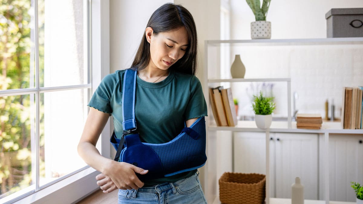woman-with-her-arm-in-a-sling-standing-by-a-window